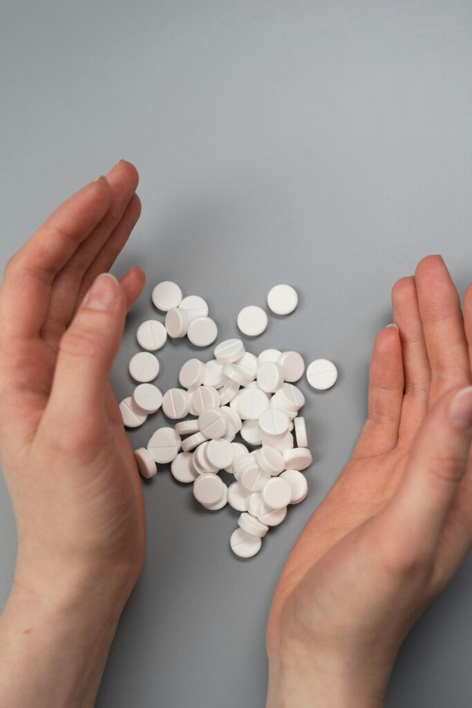 A close-up of hands near a pile of white tablets on a grey surface.