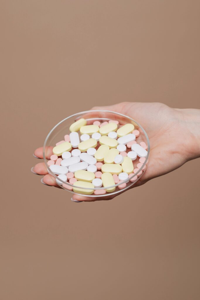 A hand holding assorted pills in a petri dish, symbolizing healthcare and treatment.